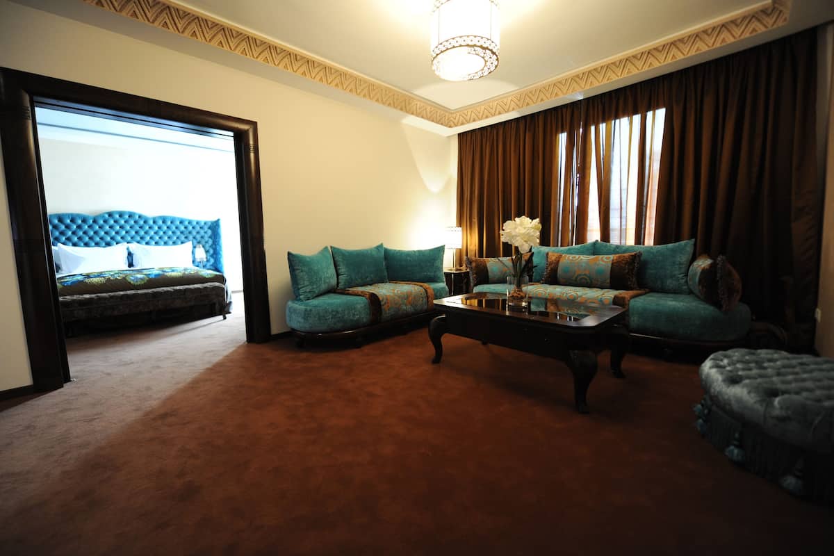 A hotel room with a large bed, a sofa set, a coffee table, and a view of the outdoors.