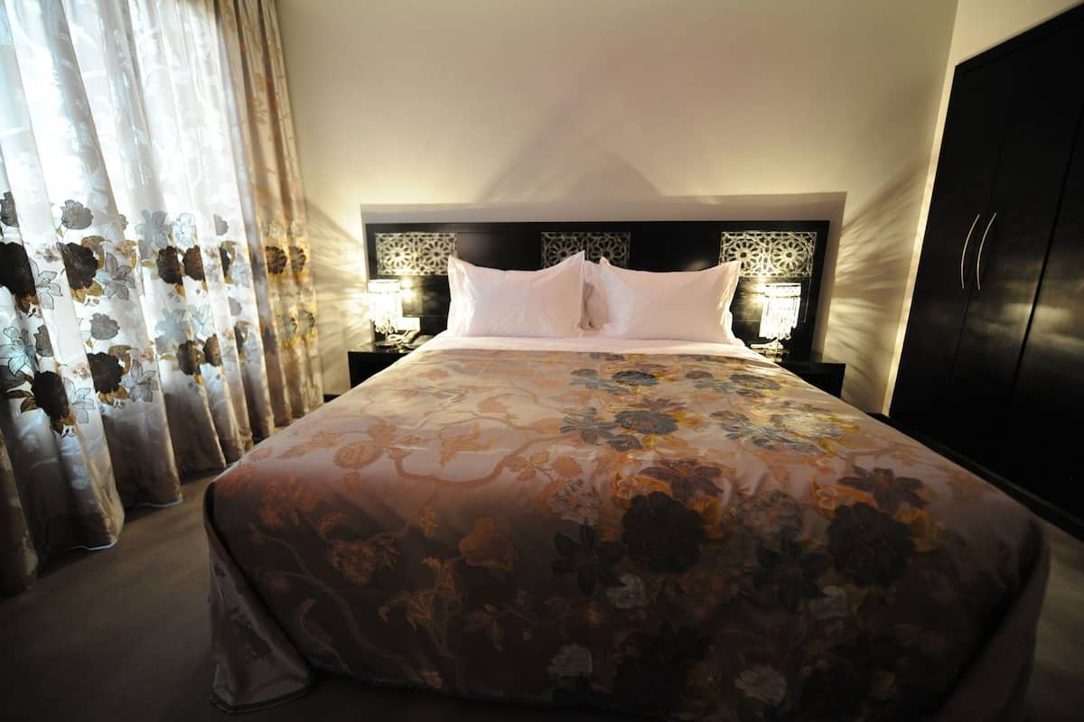 A hotel room with a large bed, floral bedspread, two bedside lamps, and a dark wardrobe.