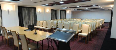 Un salón de conferencias con una mesa larga, varias sillas, un proyector y una computadora portátil.