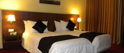 Una cama doble con ropa de cama blanca y almohadones negros, flanqueada por mesitas de noche con lámparas, en una habitación con alfombra roja y un cuadro sobre la cama.