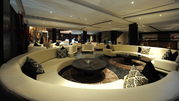 A spacious, modern lounge area with a curved white sofa, a central coffee table, and a staircase leading to an upper level.