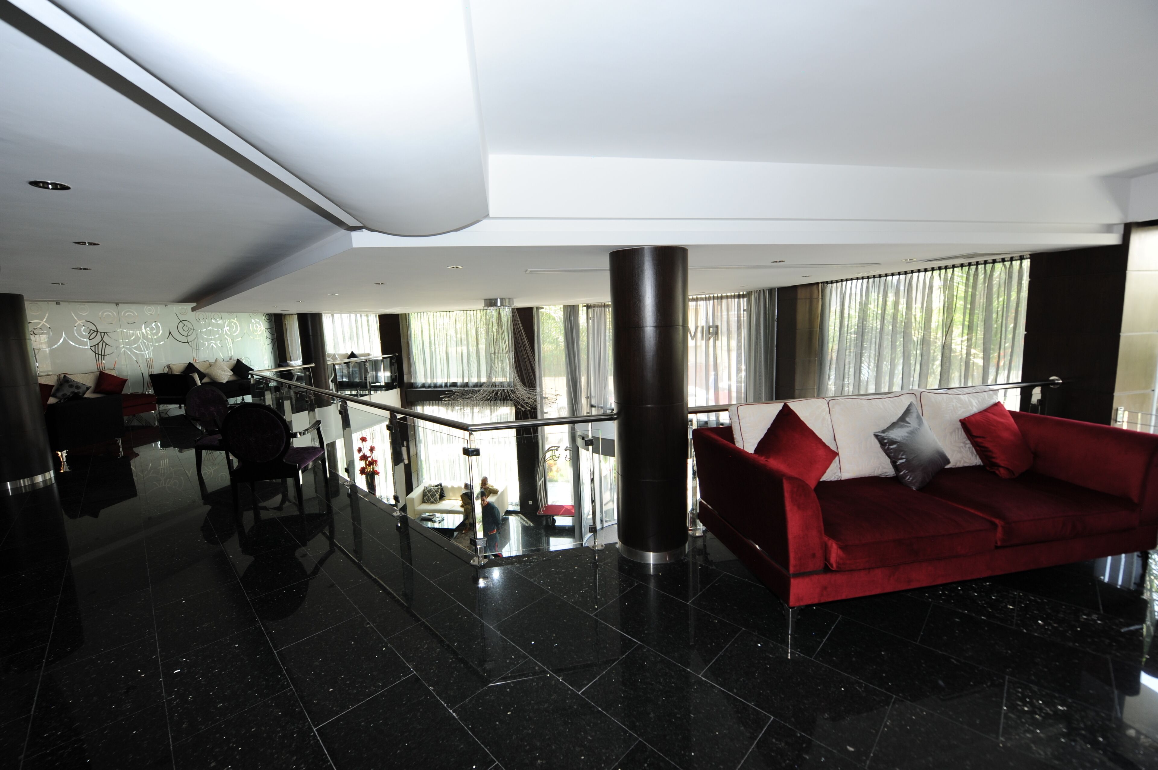 A spacious lobby with a red sofa, black tiled floor, and large windows.