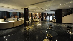 A modern hotel lobby with a curved white sofa, gold bar stools, and a staircase.
