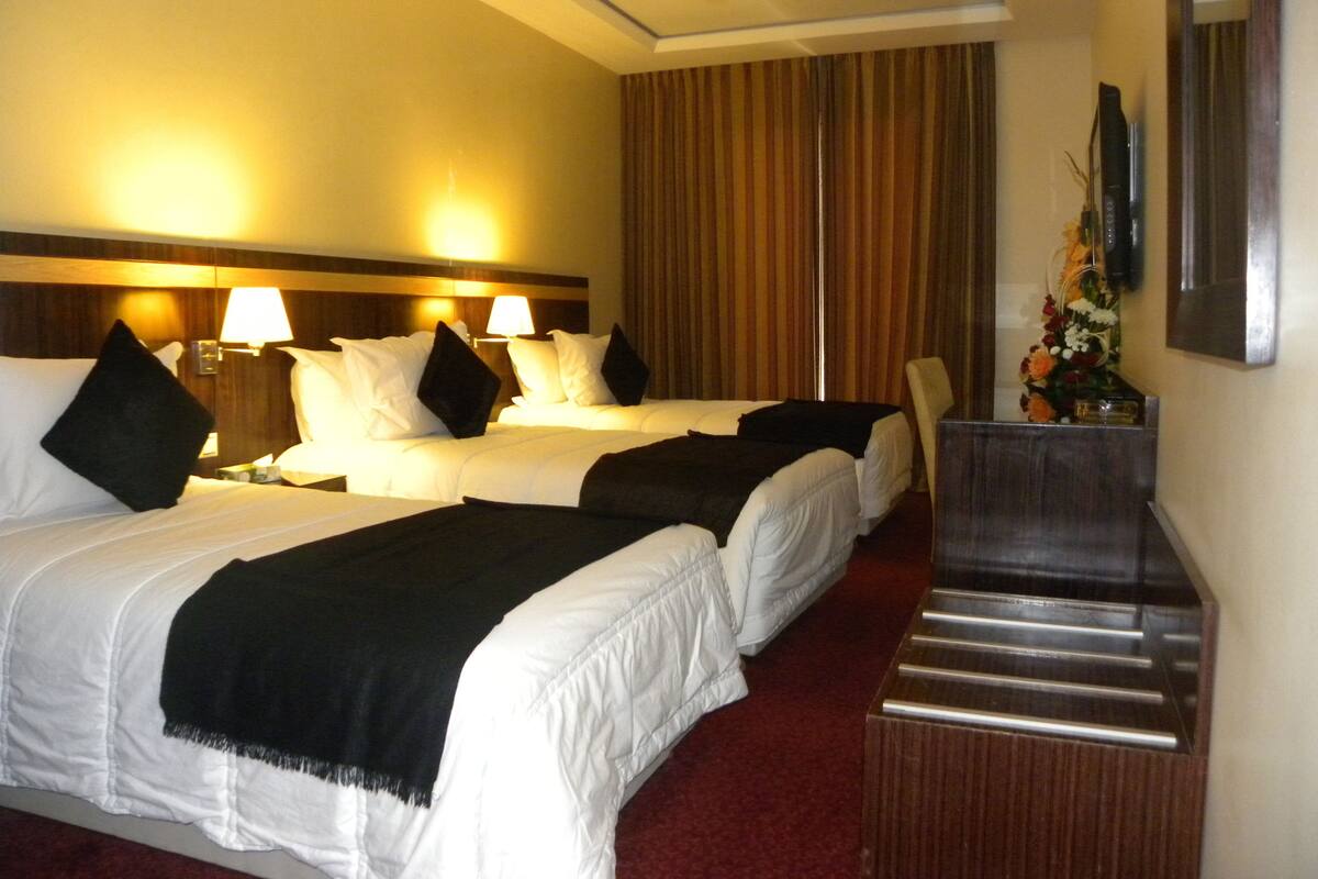 A hotel room with two beds, a wooden headboard, a desk, and a mirror.