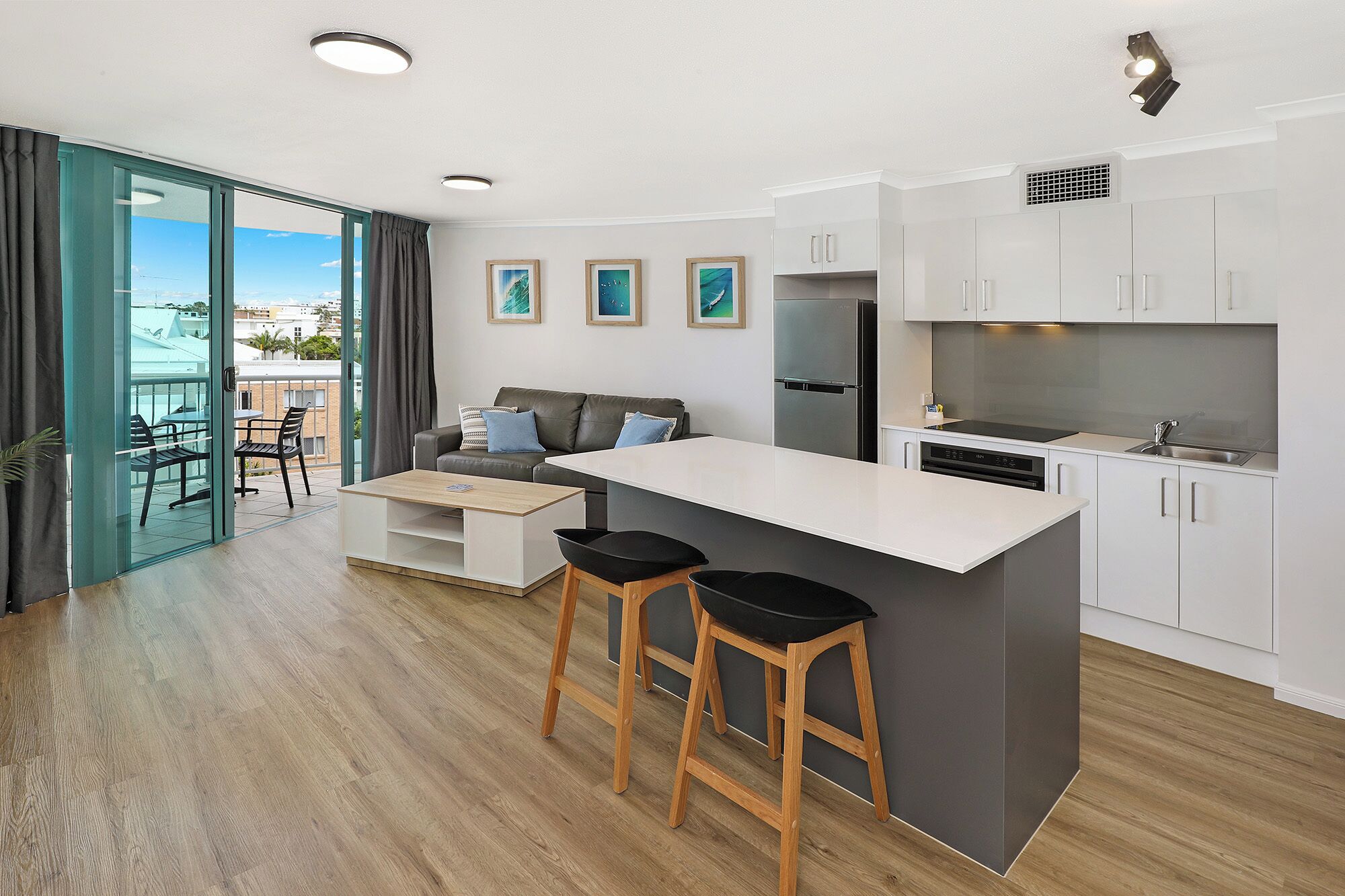 A modern kitchen with a central island, bar stools, a built-in oven, and a refrigerator.