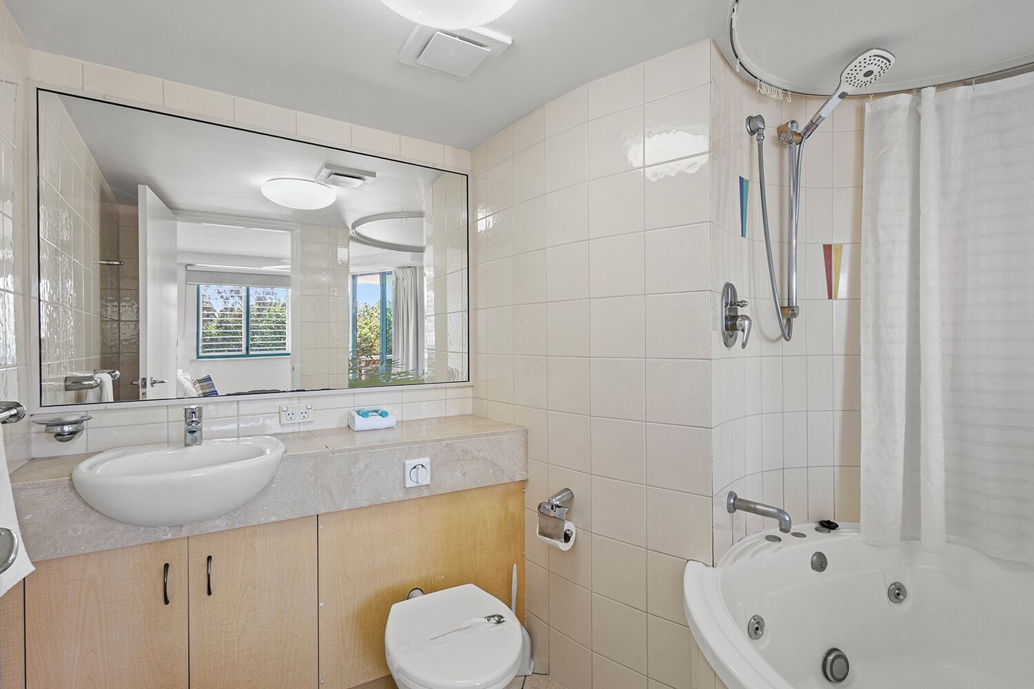Uma casa de banho moderna com um espelho grande, duas pias, uma sanita e uma banheira.