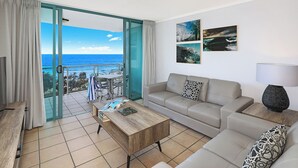 A living room with a sofa, coffee table, and a view of the ocean through a glass door. - Grand Palais Boolarong Beachside Resort (Alexandra Headland)