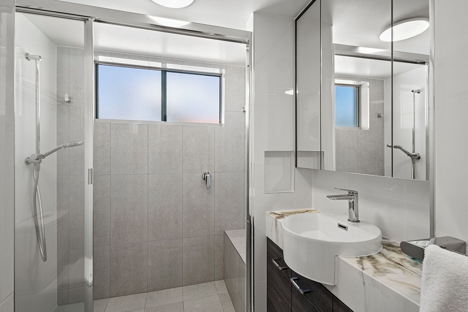 Een moderne badkamer met een douche met glazen wand, een wit wastafeltje en een grote spiegel.