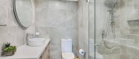 Un baño moderno con cabina de ducha de vidrio, un espejo redondo, un lavamanos y un inodoro.