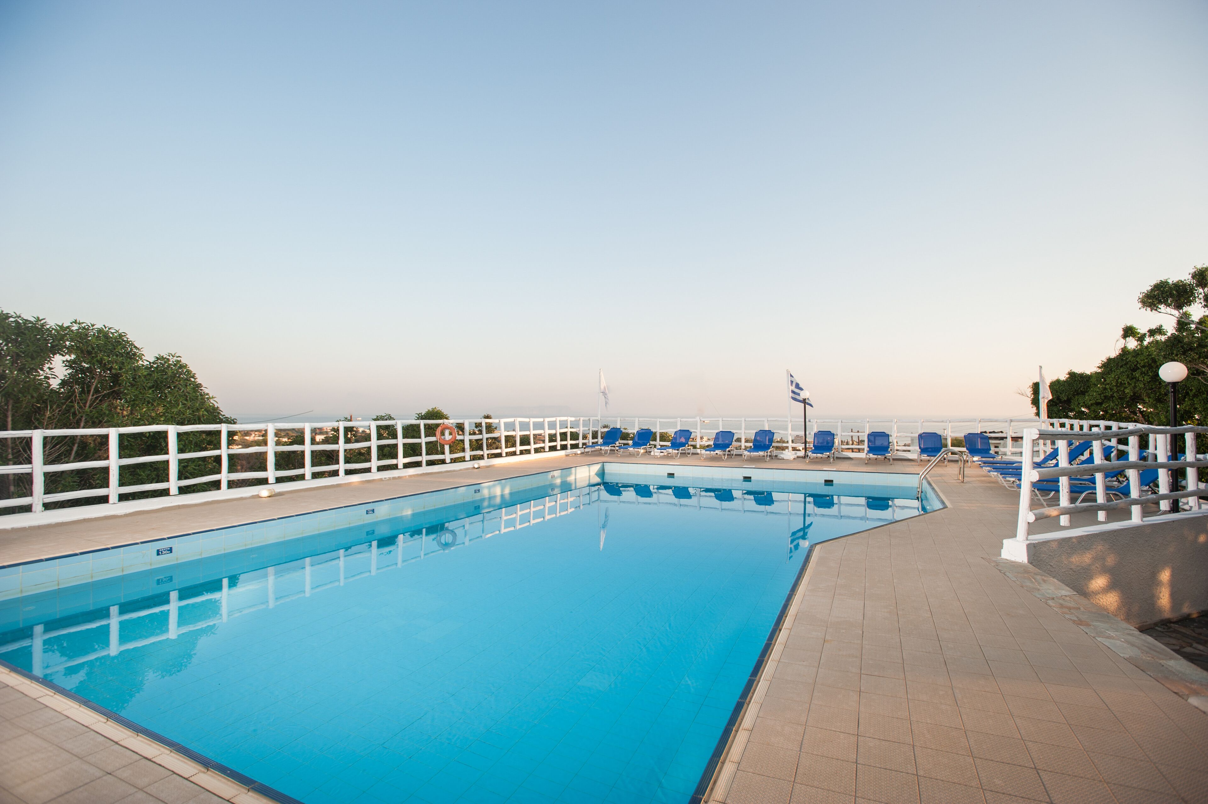 Una piscina rectangular con barandilla blanca y sillas azules a lo largo del borde.