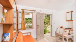 Un dormitorio con cama, una mesita de noche con un libro, una ventana con cortinas y vistas al jardín.