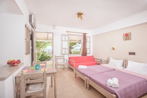 A hotel room with two beds, a desk with a chair, a small table with fruit, and a view of the outdoors. - Panorama - Sea View (Hersonissos)