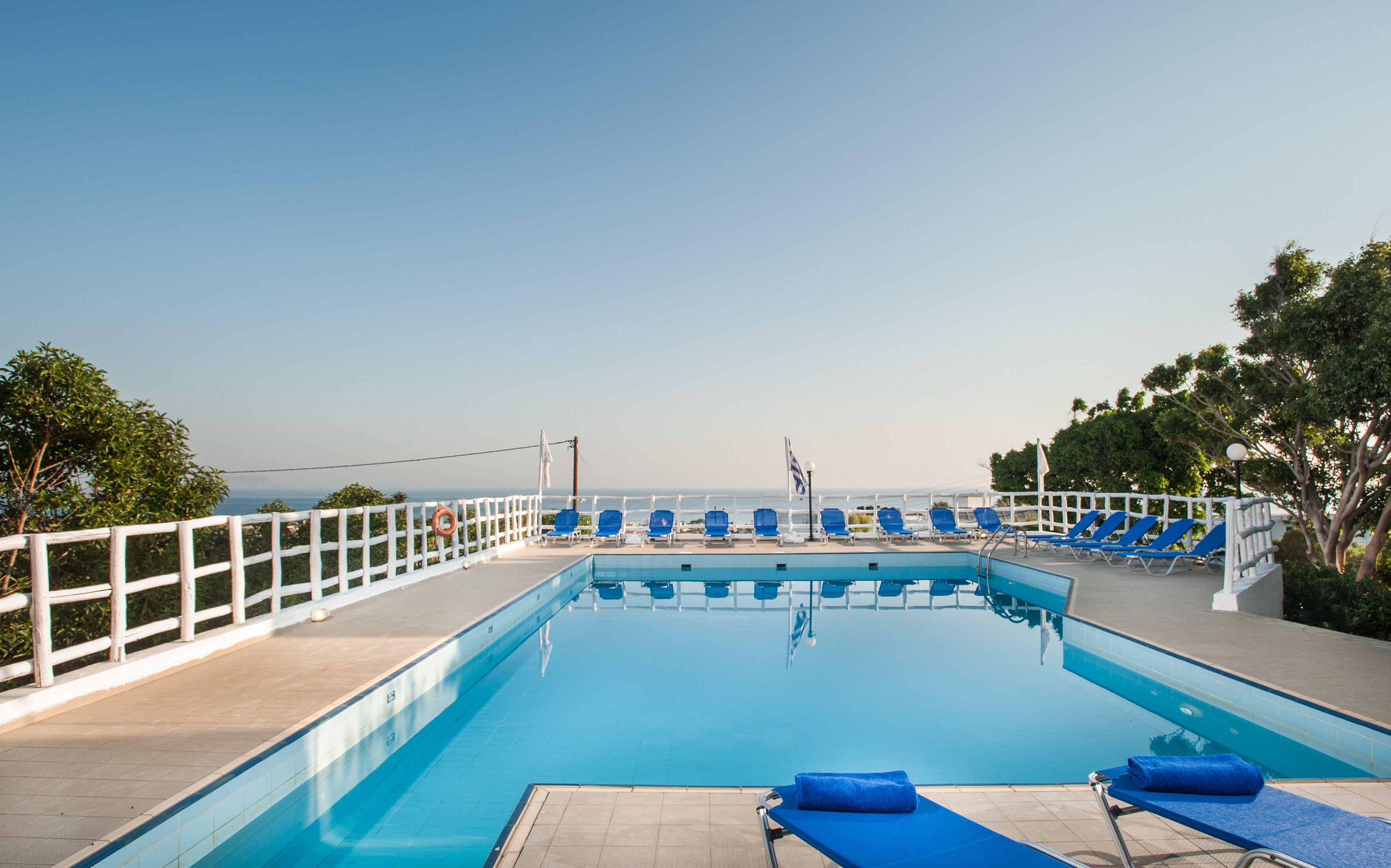 Un área de piscina con sillas reclinables azules y una cerca blanca.