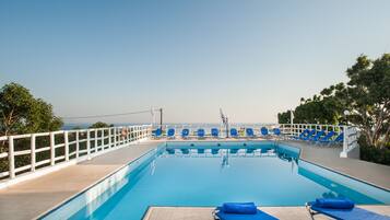 Un área de piscina con sillas reclinables azules y una cerca blanca.