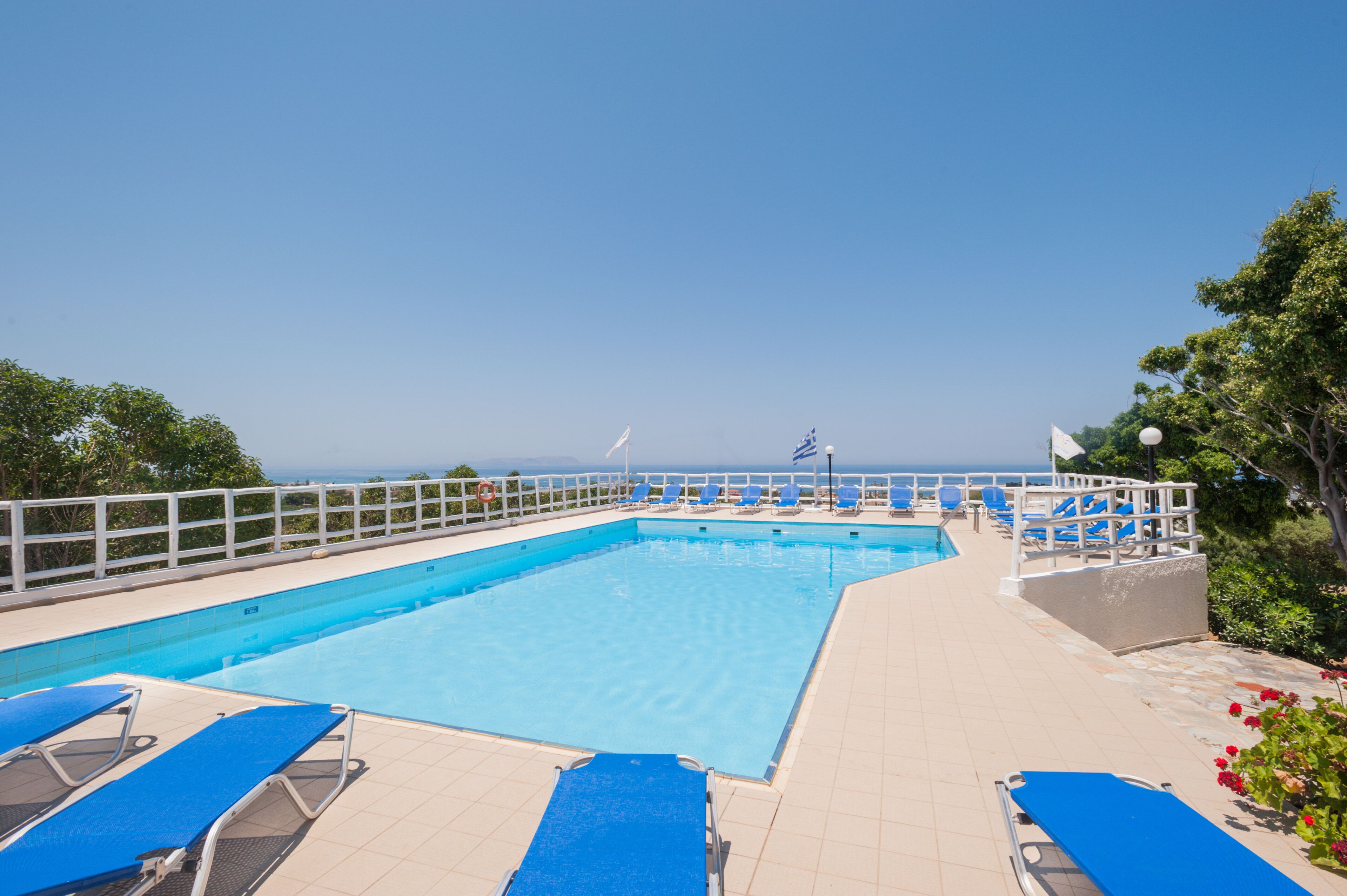 Piscina rectangular con agua azul, rodeada por una terraza blanca y sillas reclinables azules.
