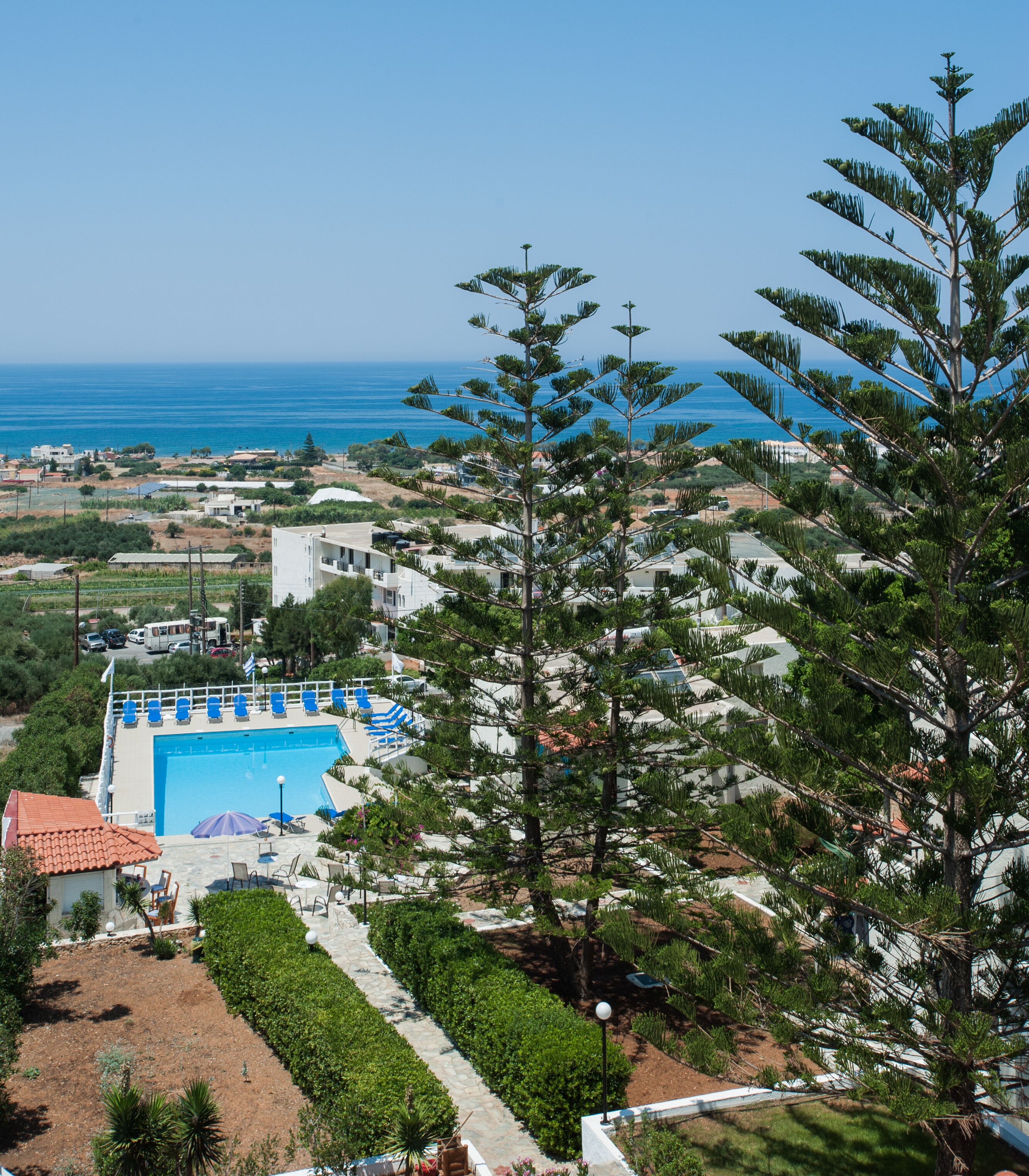 Un espace piscine offrant une vue dégagée sur la mer, entouré de verdure et de bâtiments.