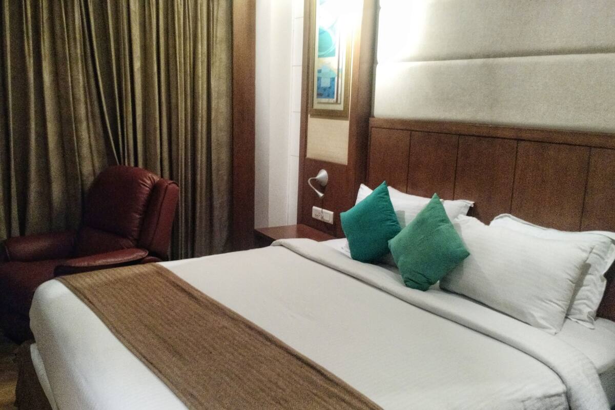 Habitación de hotel con una cama grande, cabecera de madera, manta marrón y dos almohadas verdes.