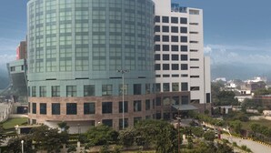 A modern building with a curved glass facade and a rectangular section with a white exterior. - Savoy Suites Greater Noida (Greater Noida)