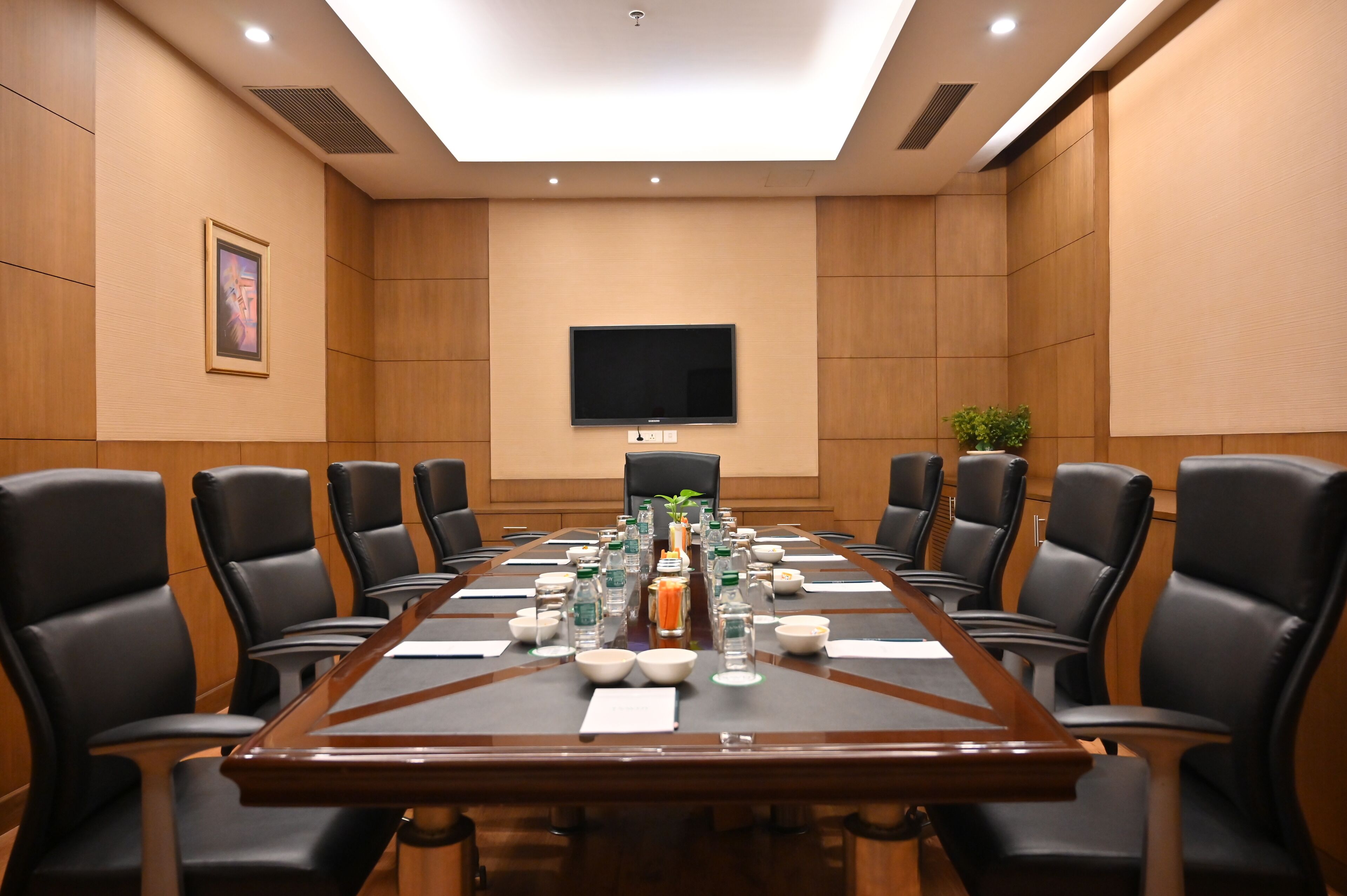 A conference room with a long table, black chairs, a flat-screen TV, and a framed picture on the wall.