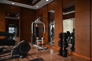 Un gimnasio con cinta de correr, máquinas de pesas y pesas sueltas.