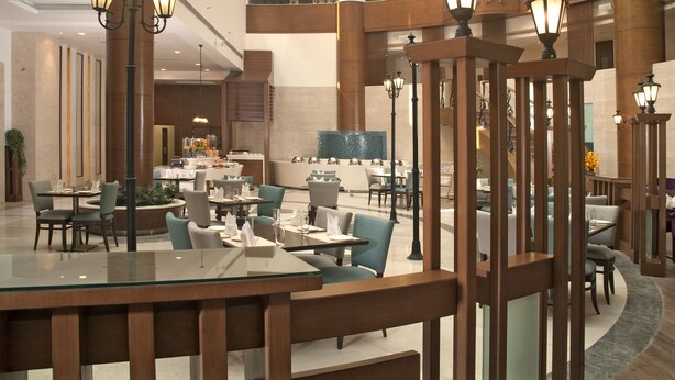 A spacious hotel lobby with multiple dining areas, large columns, and decorative lighting fixtures. - Savoy Suites Greater Noida (Greater Noida)