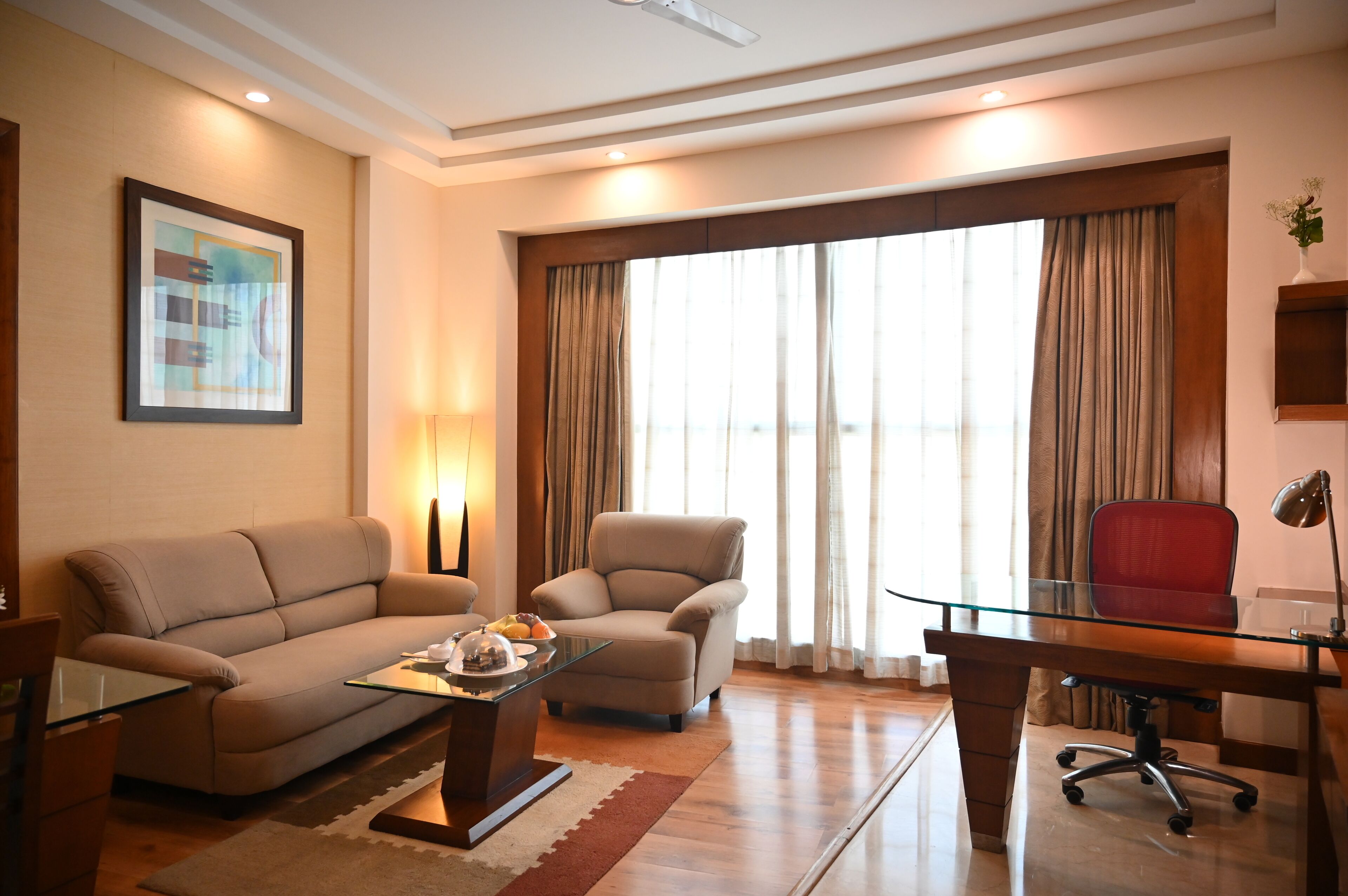 A modern living room with a sofa, armchair, glass coffee table, and a desk with a chair.