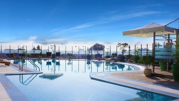A clear blue pool with a view of the ocean, surrounded by lounge chairs and potted plants. - Ramada by Wyndham Neemrana (Neemrana)