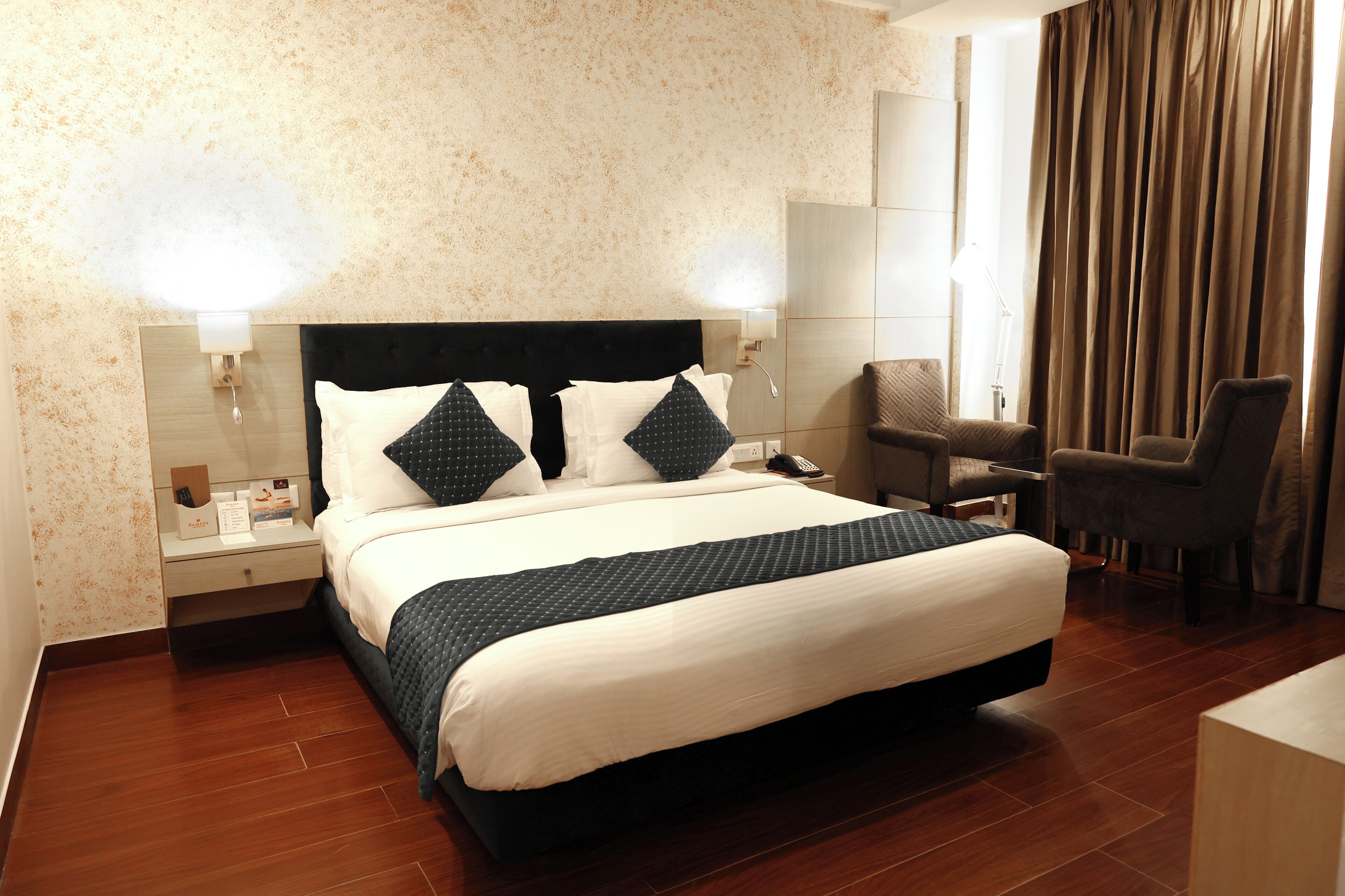 A hotel room with a bed, bedside table, lamp, chair, and a view of the outdoors.