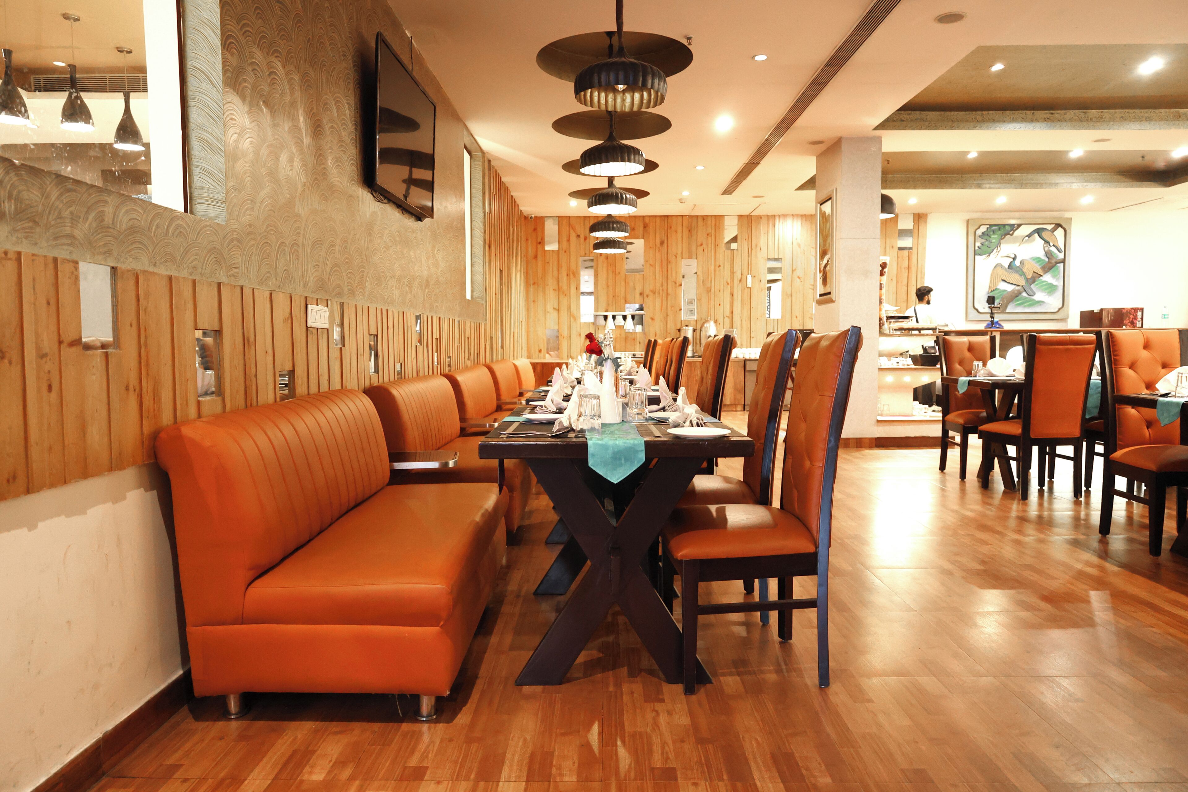 A restaurant with wooden panel walls, a long dining table, orange cushioned booths, and multiple ceiling lights.
