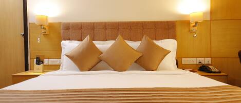 A hotel room with a large bed, two bedside lamps, a wooden headboard, and a nightstand with a telephone.
