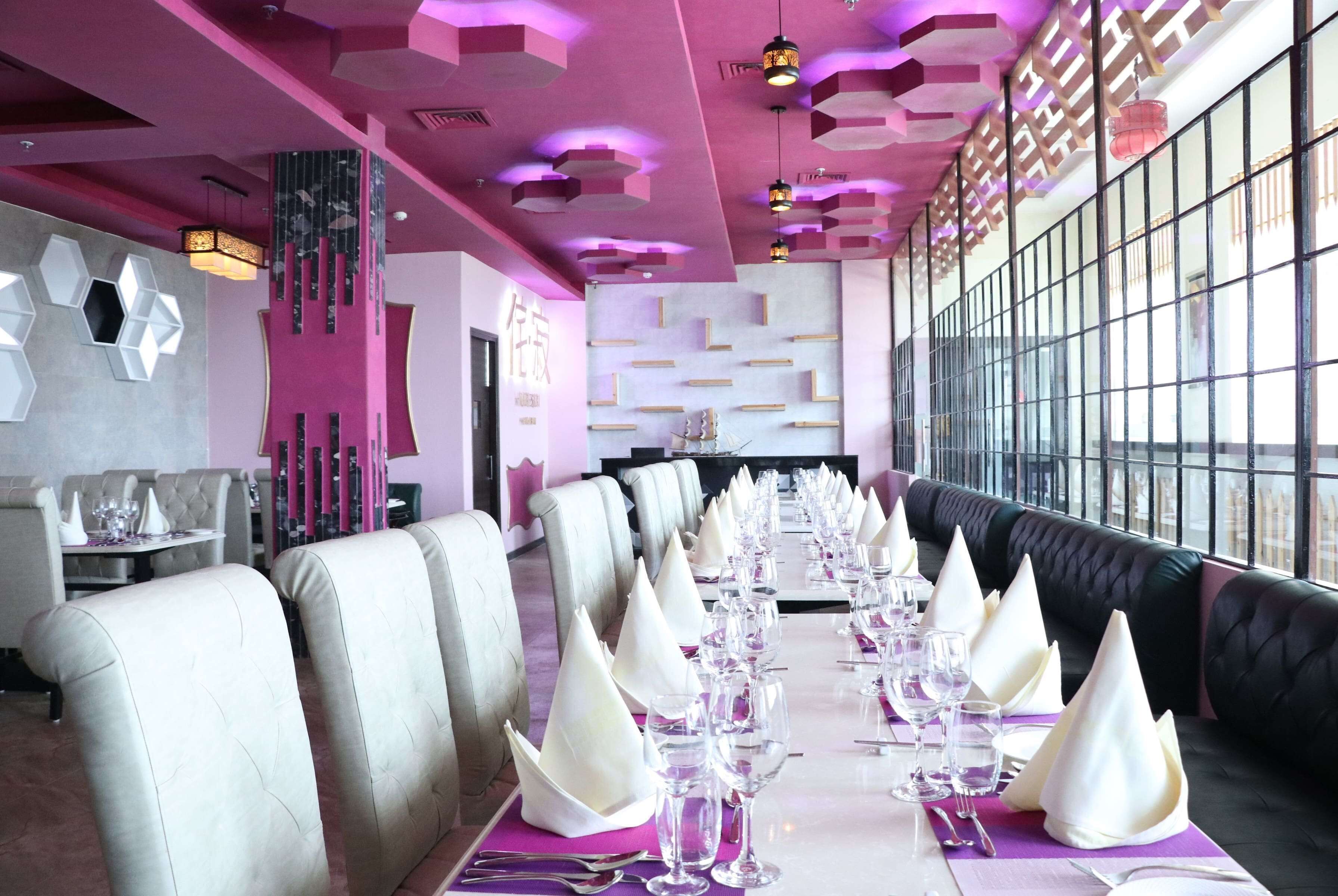 A dining area with a long table set for a formal meal, surrounded by upholstered chairs and a black leather booth.