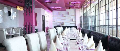 A dining area with a long table set for a formal meal, surrounded by upholstered chairs and a black leather booth.