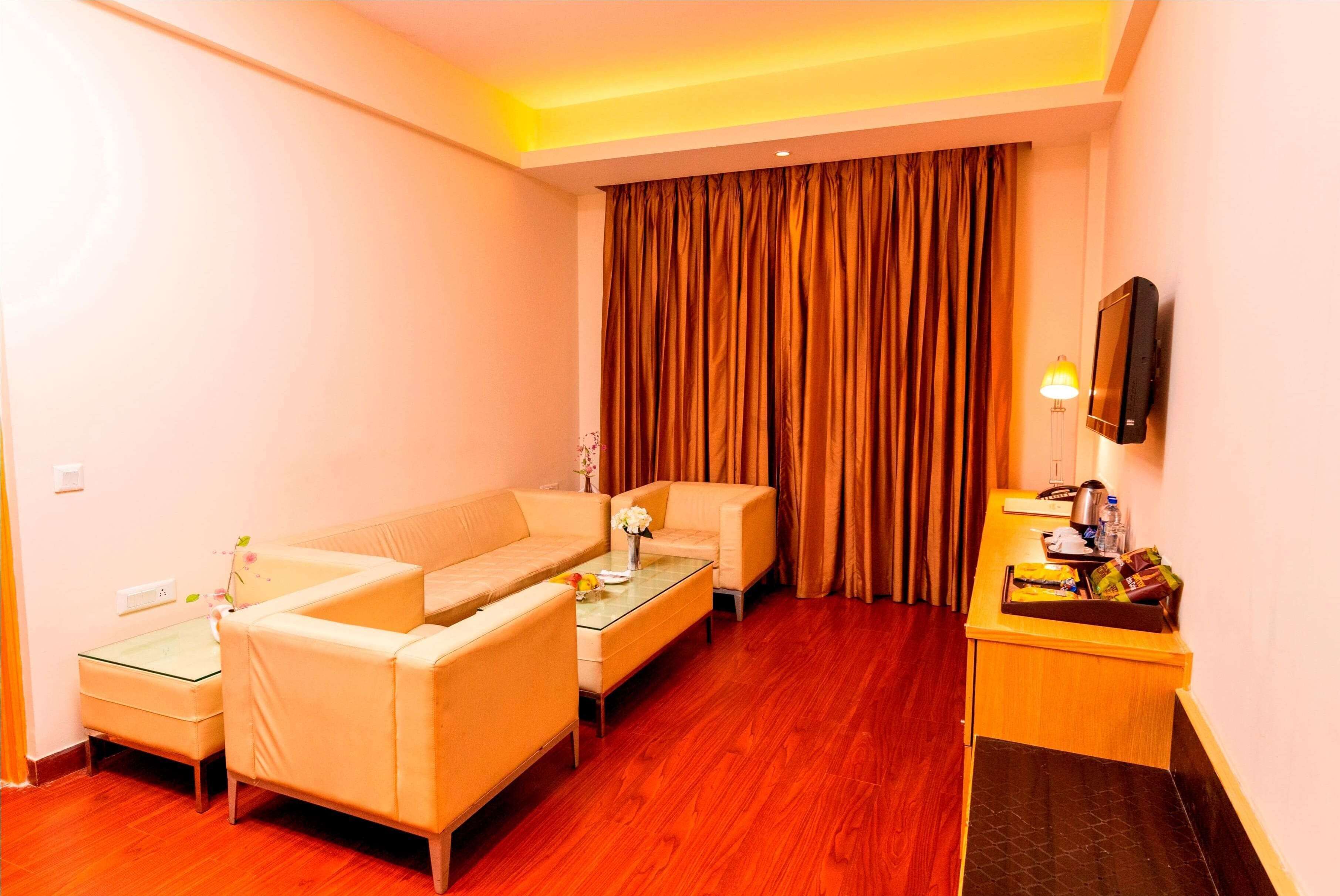A hotel room with a sofa set, a small table, a TV, and a desk with a lamp.