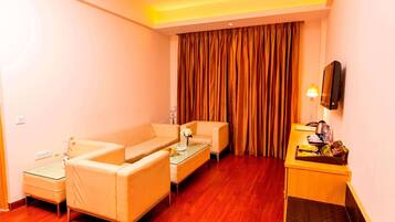 A hotel room with a sofa set, a small table, a TV, and a desk with a lamp.
