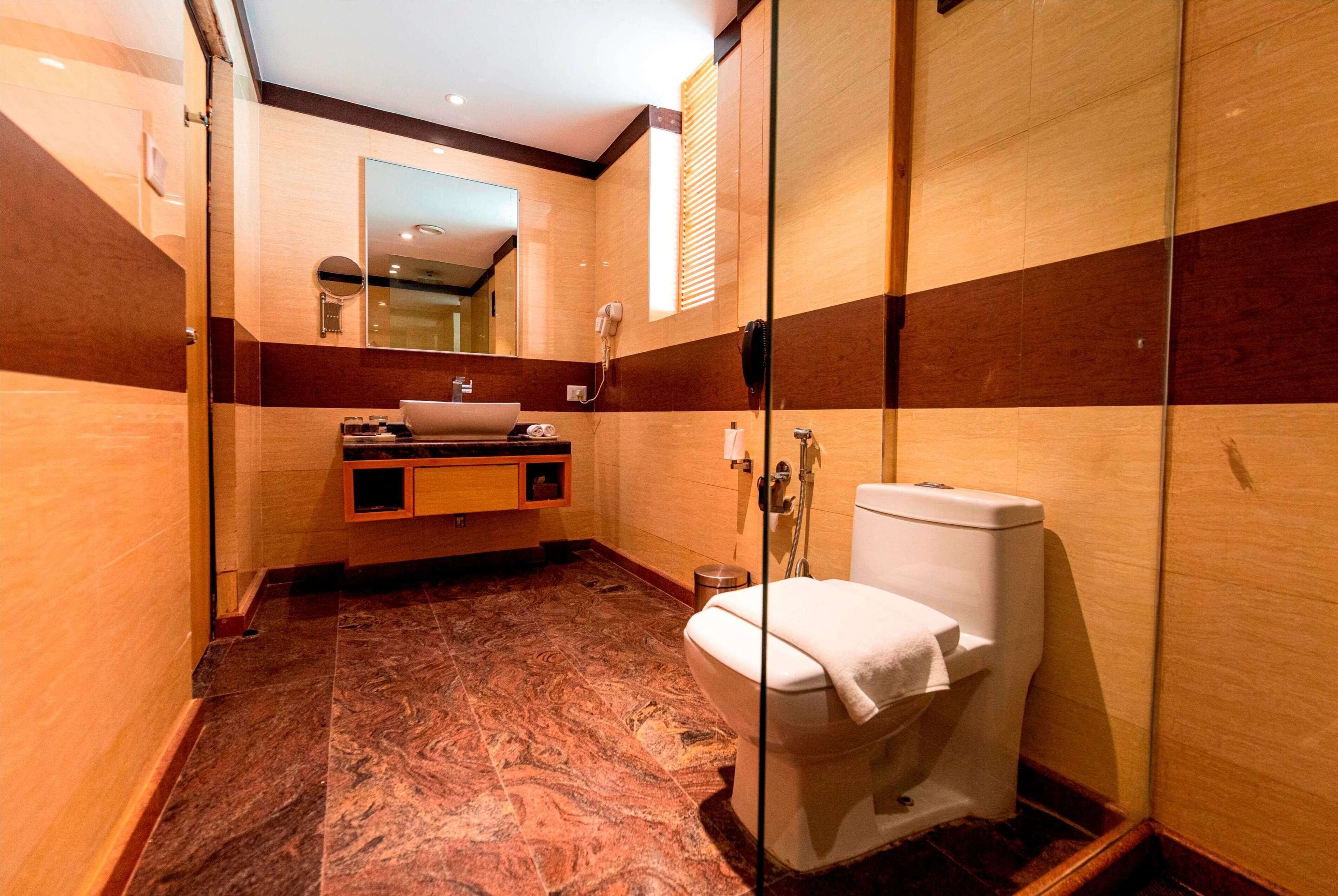 A modern bathroom with a marble floor, a wooden vanity, a glass shower enclosure, and a toilet.