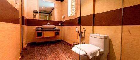 A modern bathroom with a marble floor, a wooden vanity, a glass shower enclosure, and a toilet.