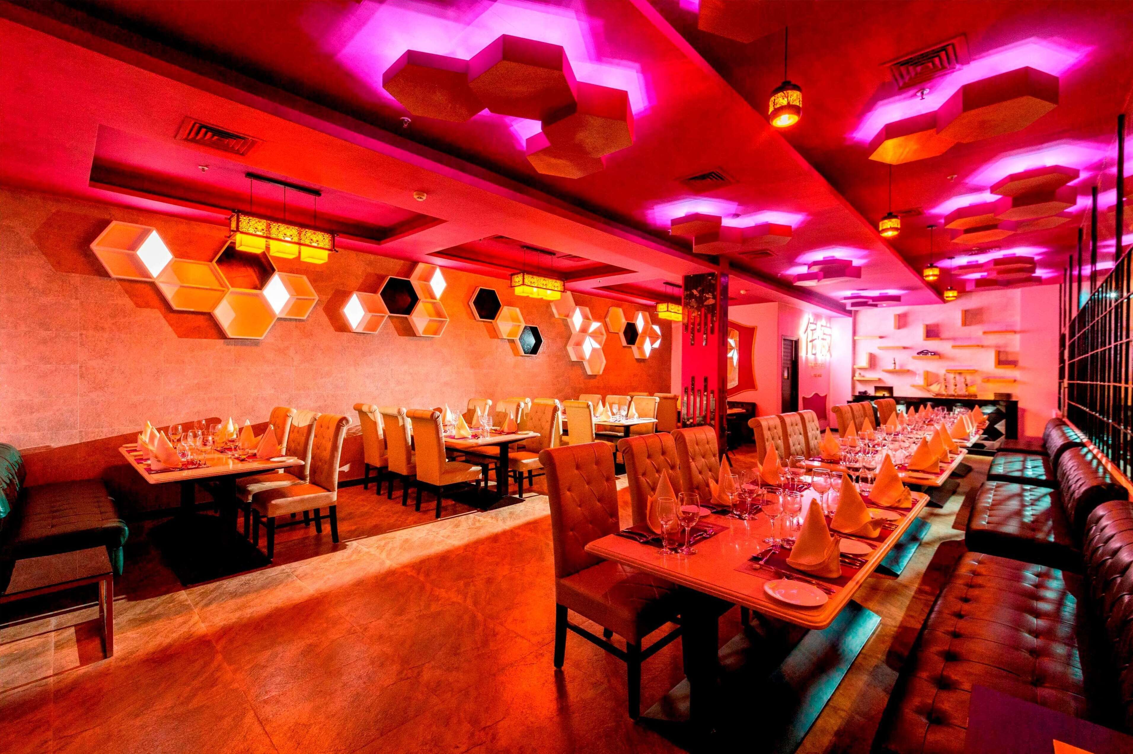 A restaurant with hexagonal light fixtures on the ceiling, wooden tables, and leather seating.