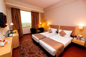 Two double beds with striped bedspreads, a desk, and a flat-screen TV.