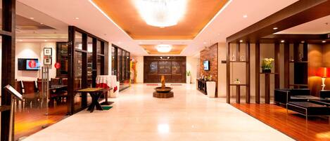 A spacious lobby with a modern design, featuring a central fountain, seating areas, and a reception desk.