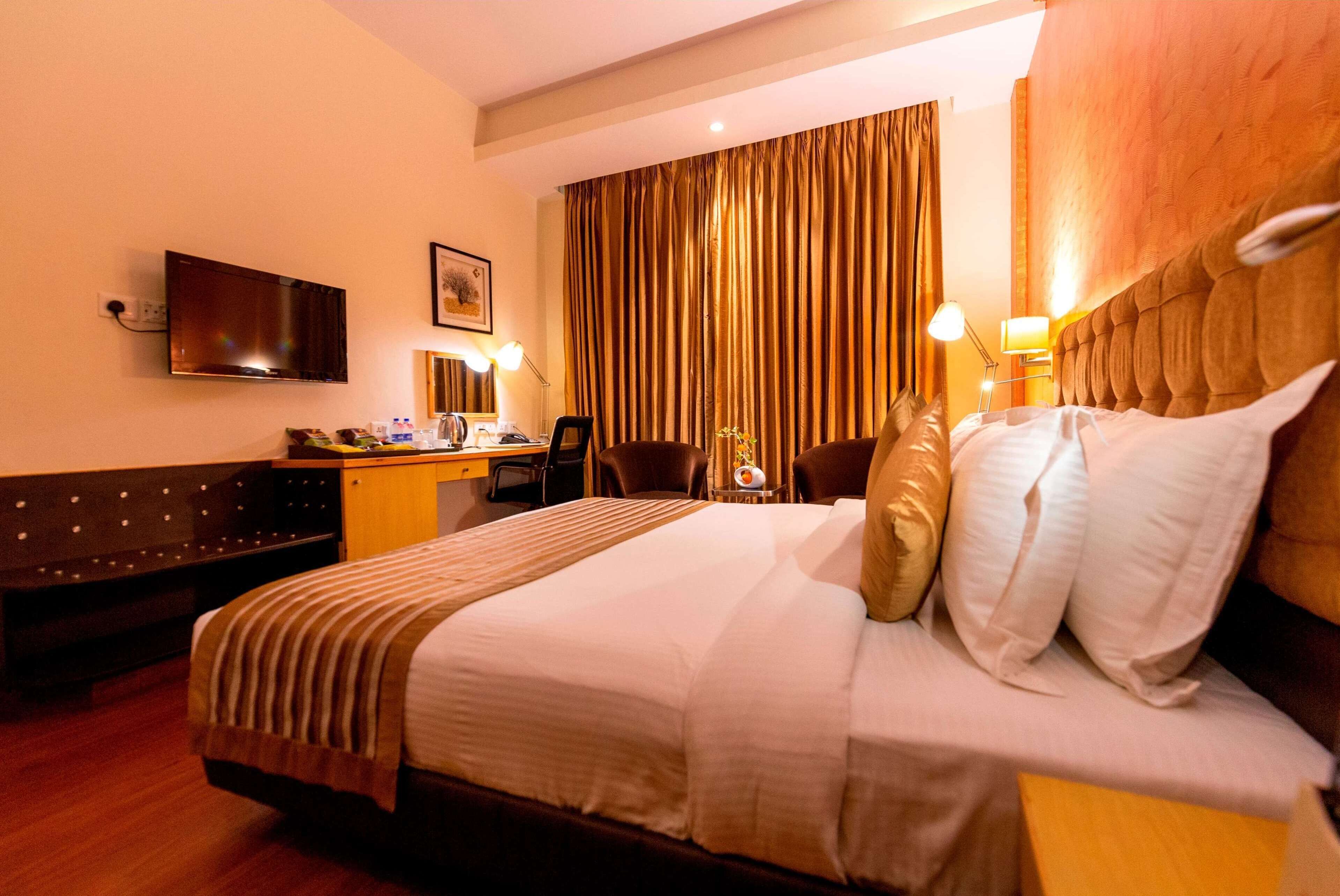 A hotel room with a large bed, a desk, a chair, a television, and a window with curtains.