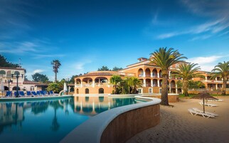 A resort with a swimming pool, palm trees, and a building with multiple balconies.