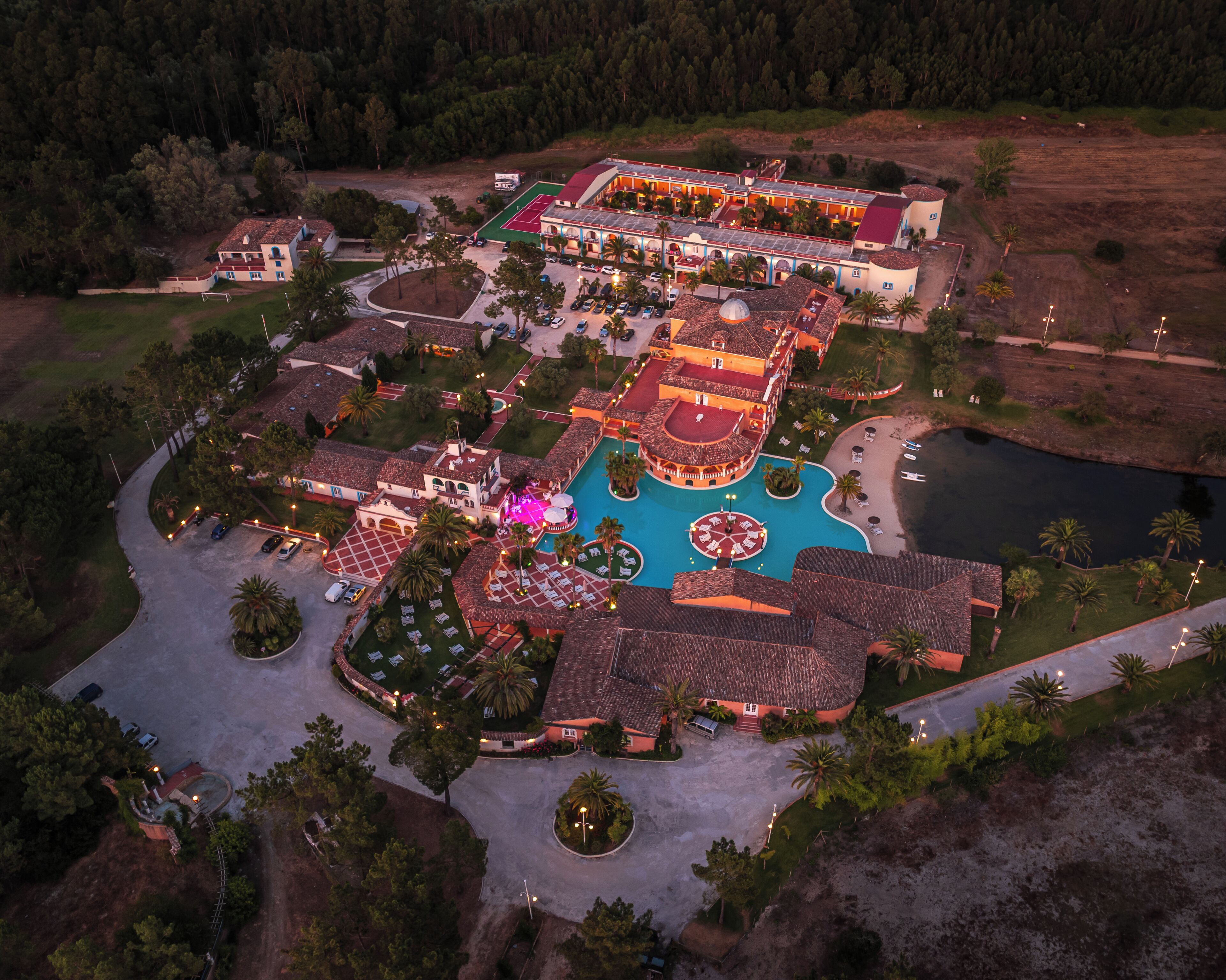 An aerial view of a resort with multiple buildings, a swimming pool, and surrounding greenery.
