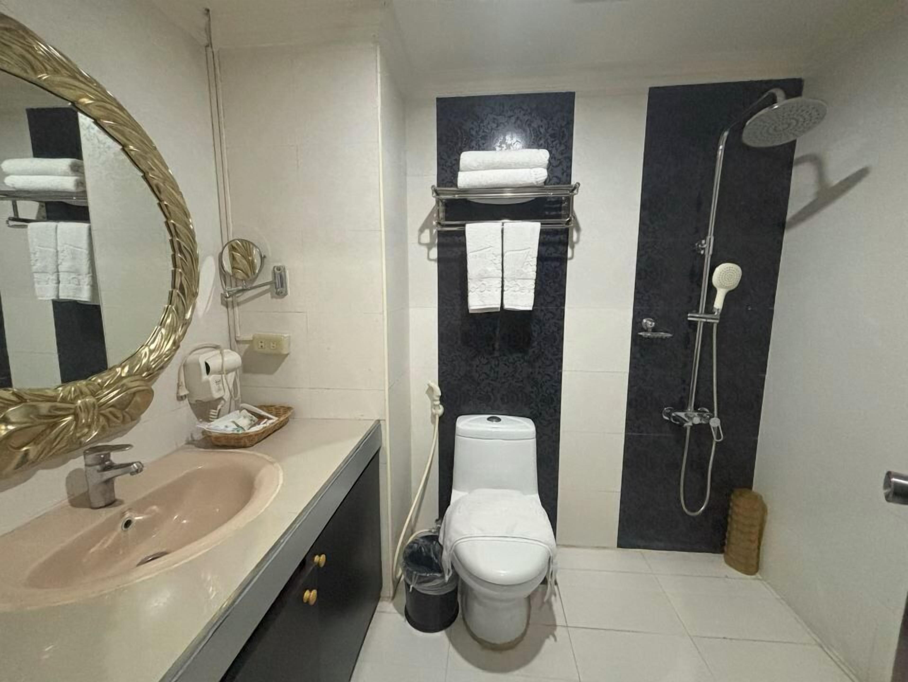 Un baño moderno con lavamanos, inodoro y ducha. Hay un perchero sobre el inodoro y un espejo con marco dorado.