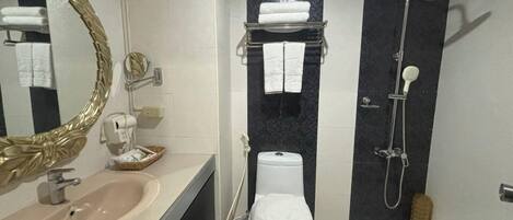 Un baño moderno con lavamanos, inodoro y ducha. Hay un perchero sobre el inodoro y un espejo con marco dorado.