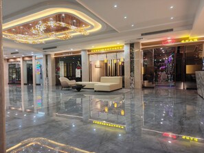 A modern lobby with a marble floor, a central seating area, and a decorative chandelier.