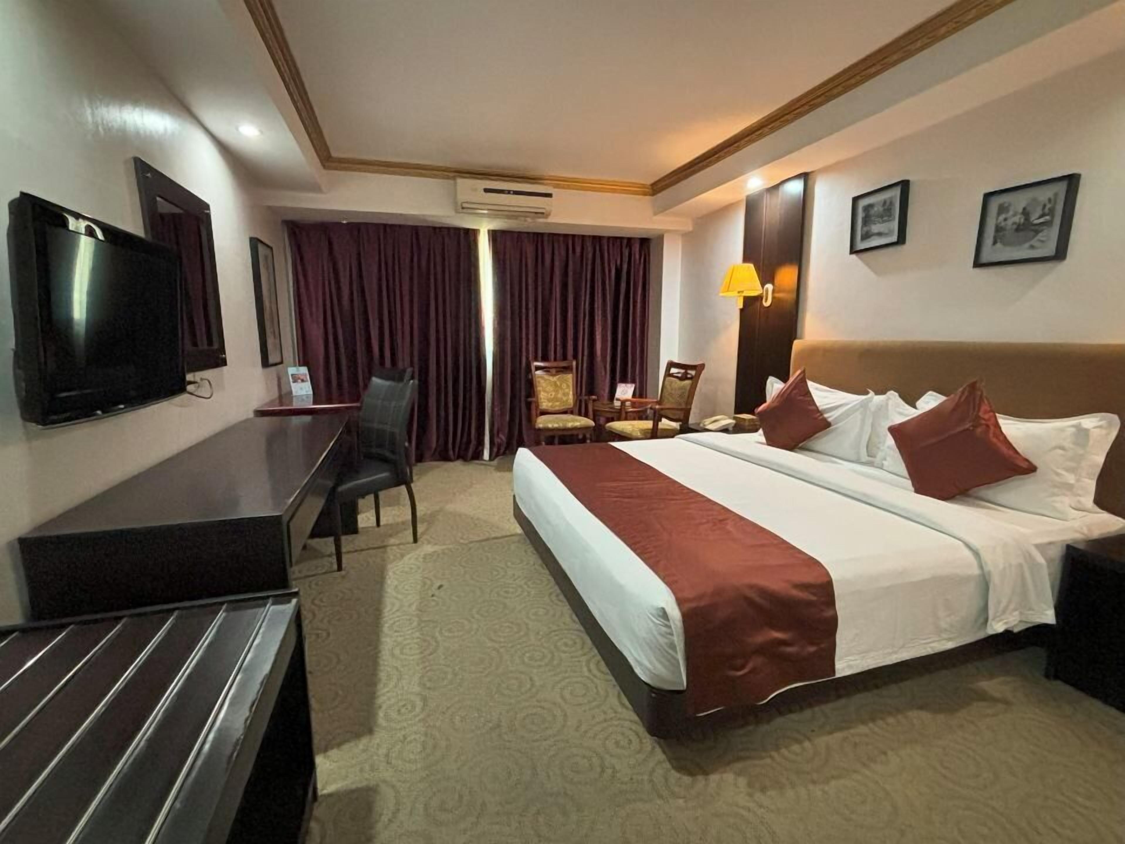 Ein Hotelzimmer mit einem Bett, einem Schreibtisch, einem Sessel, einem Fernseher und einer Wand-Klimaanlage.