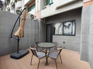 A patio area with a round table and four chairs, a standing fan, and a covered umbrella.