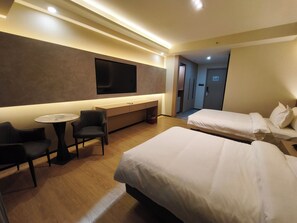 A hotel room with two beds, a desk, a chair, a TV mounted on the wall, and a small table.