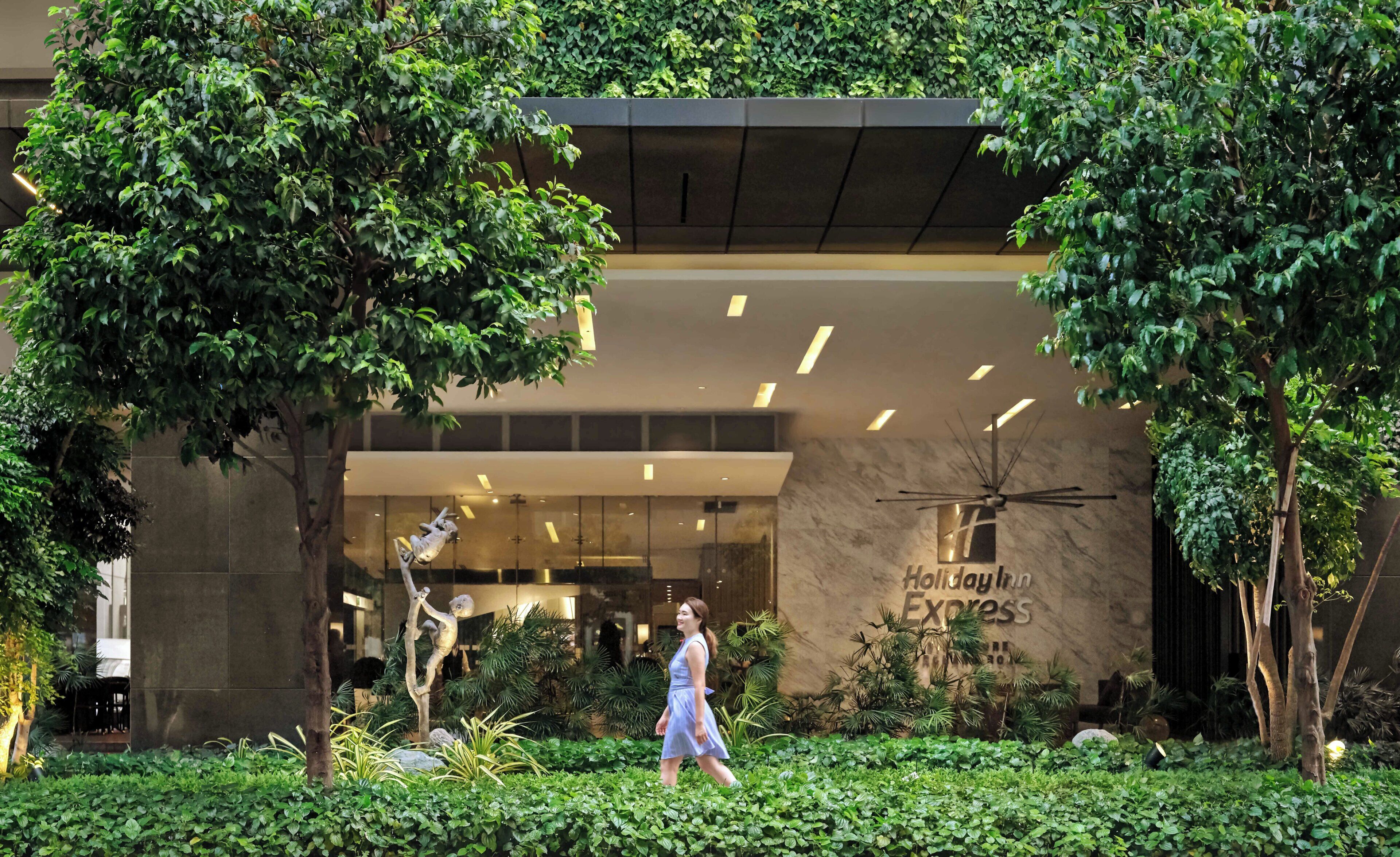 A hotel entrance with a modern design, a sign for 'Holiday Inn Express,' and a person walking in the foreground.