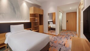 Ett hotellrum med en säng, hyllor i trä, ett skrivbord och ett badrum som syns genom en dörr.